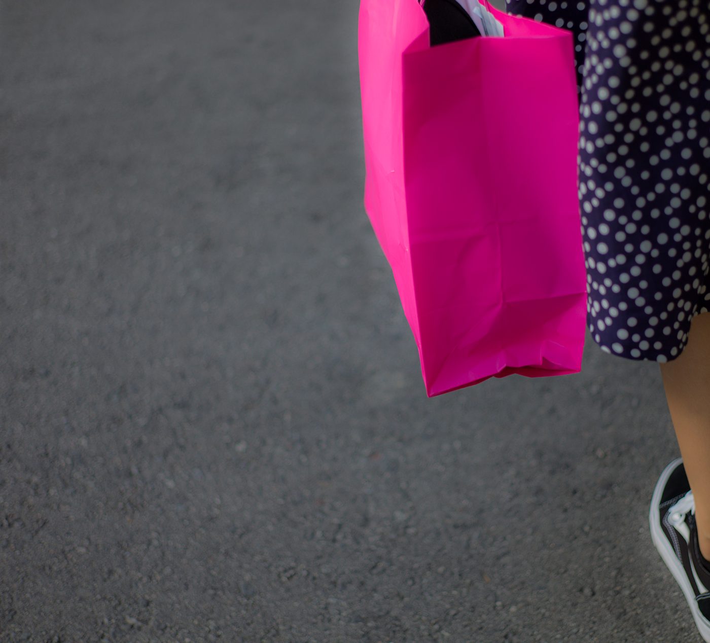 A pink shopping bag and polka-dot skirt on grey pavement